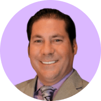 Mike Pfeffer, a man smiling in a tan suit, lavender shirt, and patterned tie, shown against a light purple circular background.